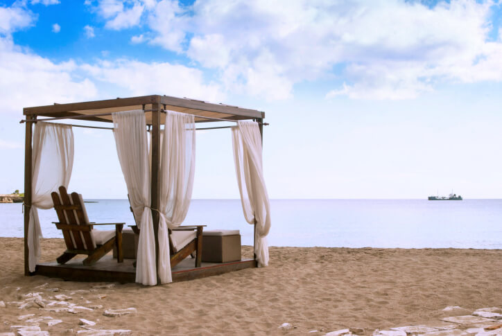 一个正方形的藤架风格的凉亭，配有透明的窗帘和阿迪朗达克椅。露台俯瞰水面，拥抱海滩的美感。