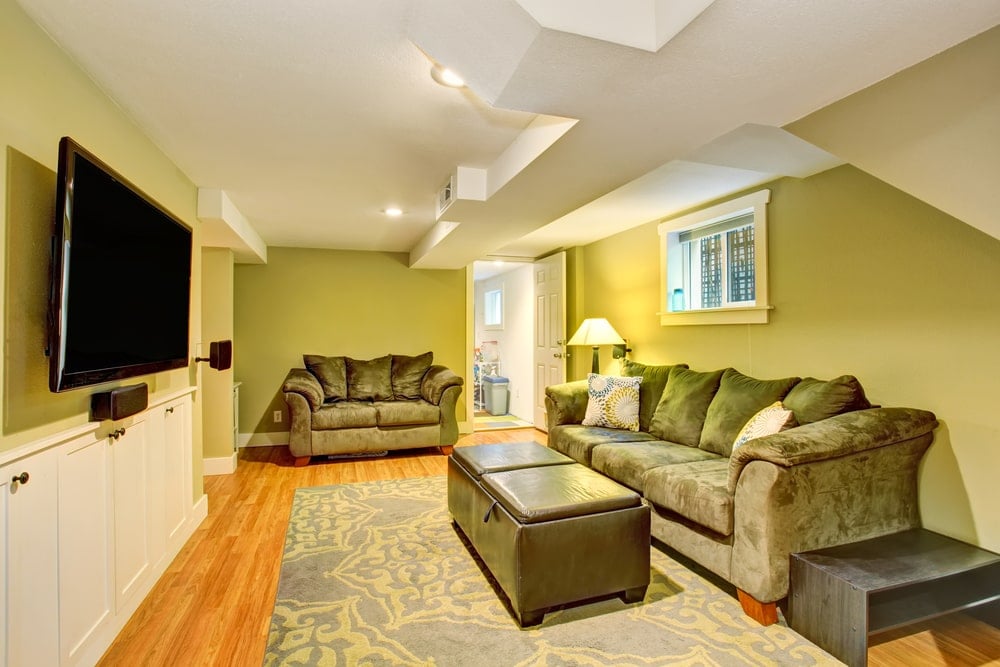这间家庭娱乐室有绿色的墙壁、灰色的沙发和与护墙板相配的白色天花板。