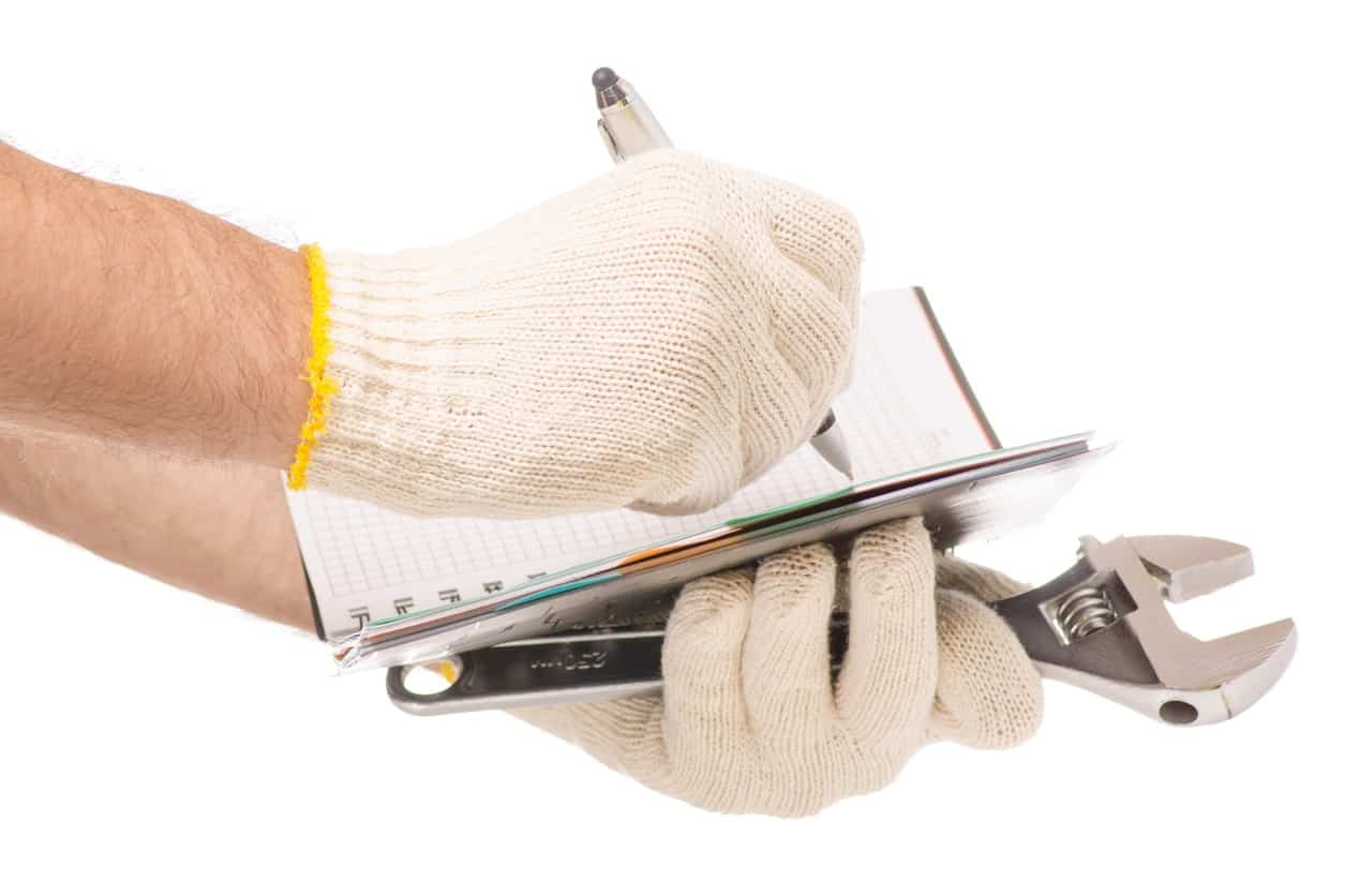 戴着防护手套在笔记本上写字，拿着工具。