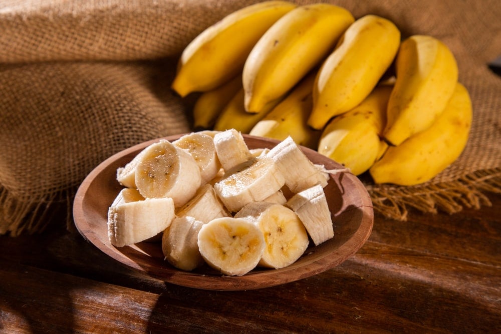 一捆成熟的香蕉和切好的香蕉放在木碗里。