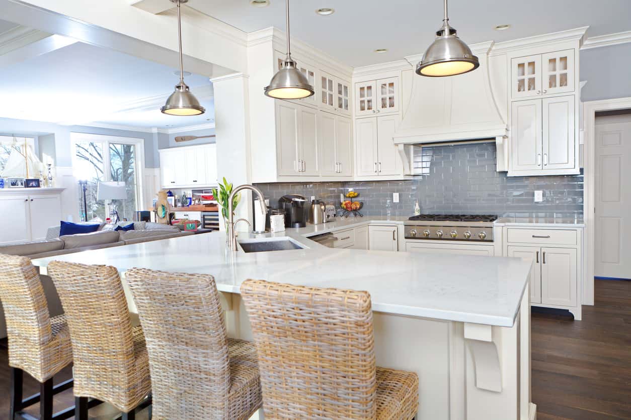 白色厨房镀铬吊灯，蓝色后挡板，深色硬木地板和柳条早餐吧台凳。
