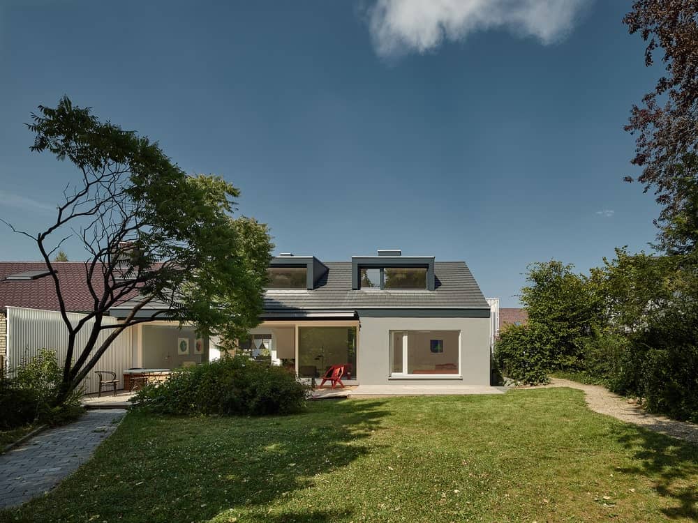 这是一个看着郊区房子的背面，有一个大草草坪，灰色的外墙，玻璃和现代的天窗窗户。