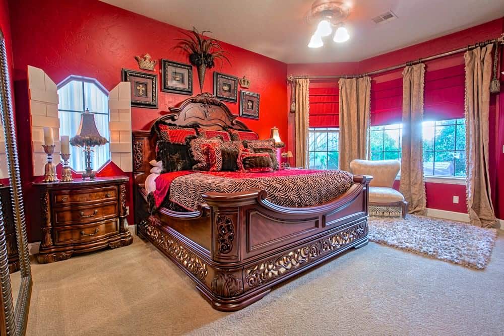 一间折衷主义卧室，包括豪华的床铺设置，周围环绕着红墙和地毯的地板。床两侧有台灯。