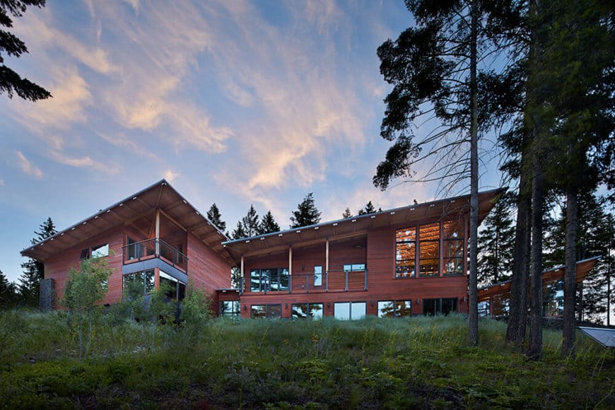 一个带红色外观的大型现代化的房子，周围环绕着成熟的树木。
