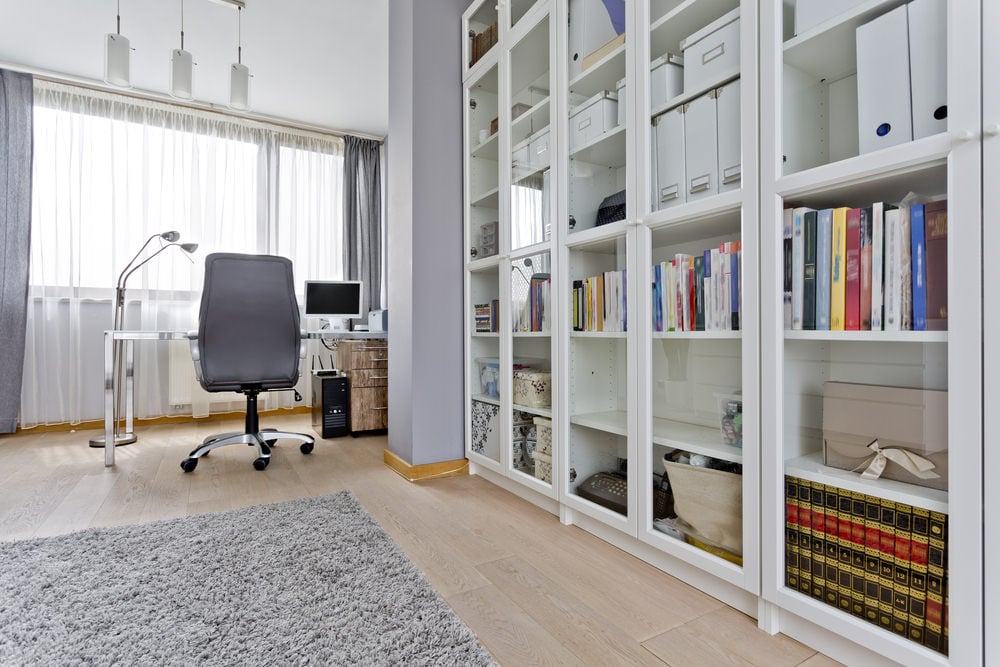 一个时髦的家庭图书馆，办公室的桌子和椅子设置在角落。白色的书架被玻璃门保护着。