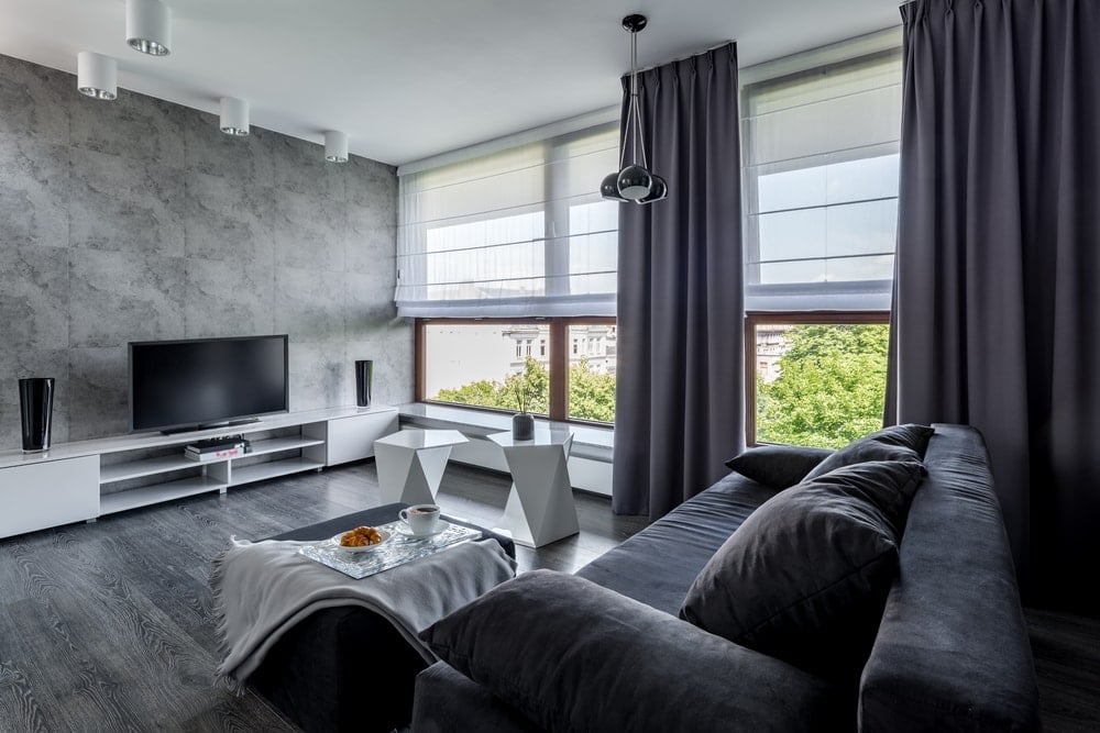 这是一间家庭娱乐室，灰色的墙壁与深灰色的地板和沙发相匹配，都被窗户的自然光照亮。