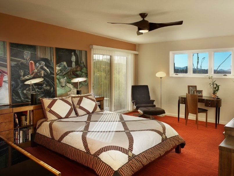 这个主卧室以房间的橙色墙壁上的艺术装饰而自豪。它采用时尚台灯照明的床铺设置。