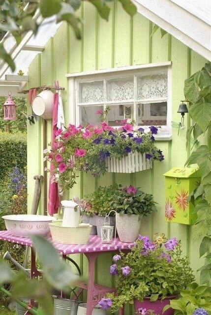 一个可爱的春天的绿色花园的小棚里有很多的鲜花和园艺配件的容器的装饰起来。粉红色的小表贴靠在一个外壁，一个伟大的工作站！