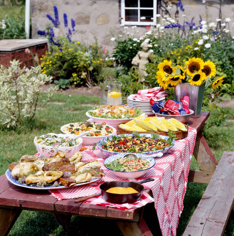这张全木的野餐桌是用格子台布装饰起来的，上面装着适合一个大家庭吃的饭菜!