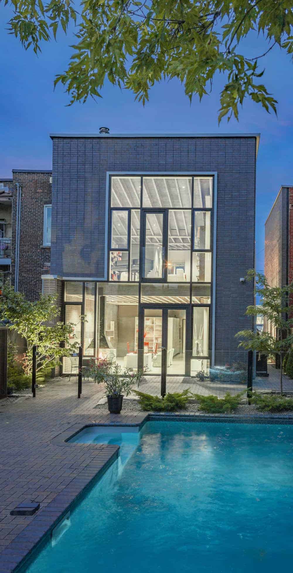 这座现代住宅有着灰色的外观，其特点是砖砌走道，周围环绕着健康的植物和树木。该住宅还带有一个游泳池。