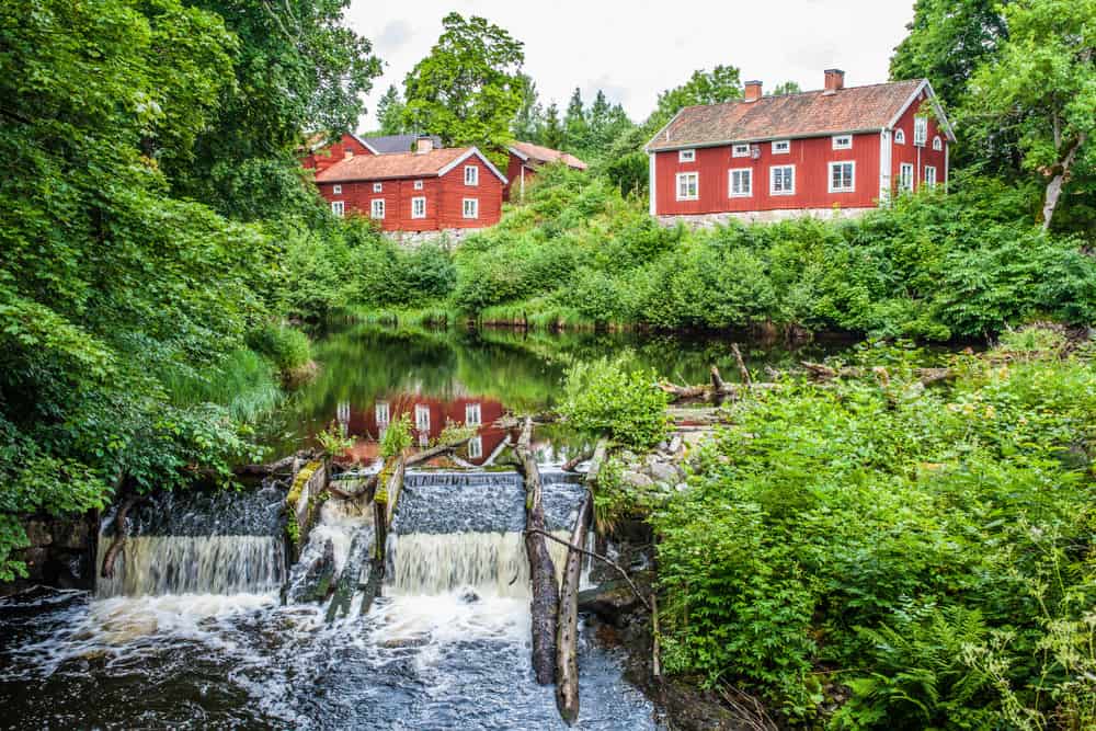 瑞典的几栋红色房屋，旁边是一条被茂密的植被环绕的小河。