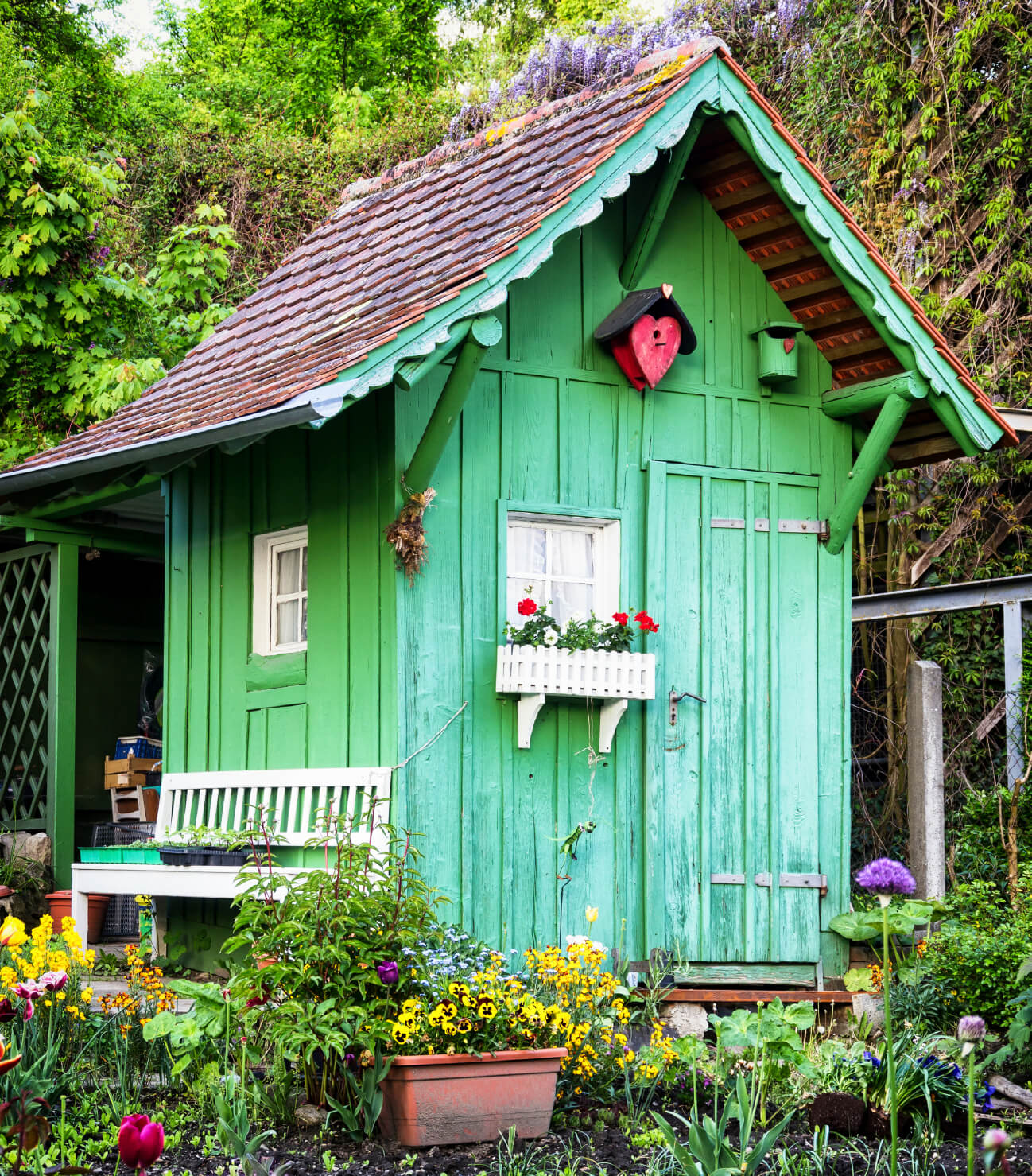 这座摇摇欲坠的花园小屋被漆成明亮的绿色，与周围的种植床形成鲜明的对比。在明亮的绿色映衬下，一个小小的尖桩窗台盒和一条配套的长凳显得格外醒目。